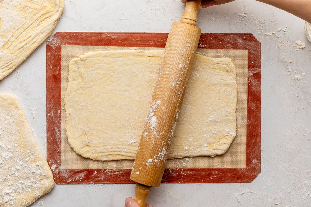 hands rolling folded dough on silicone baking mat.