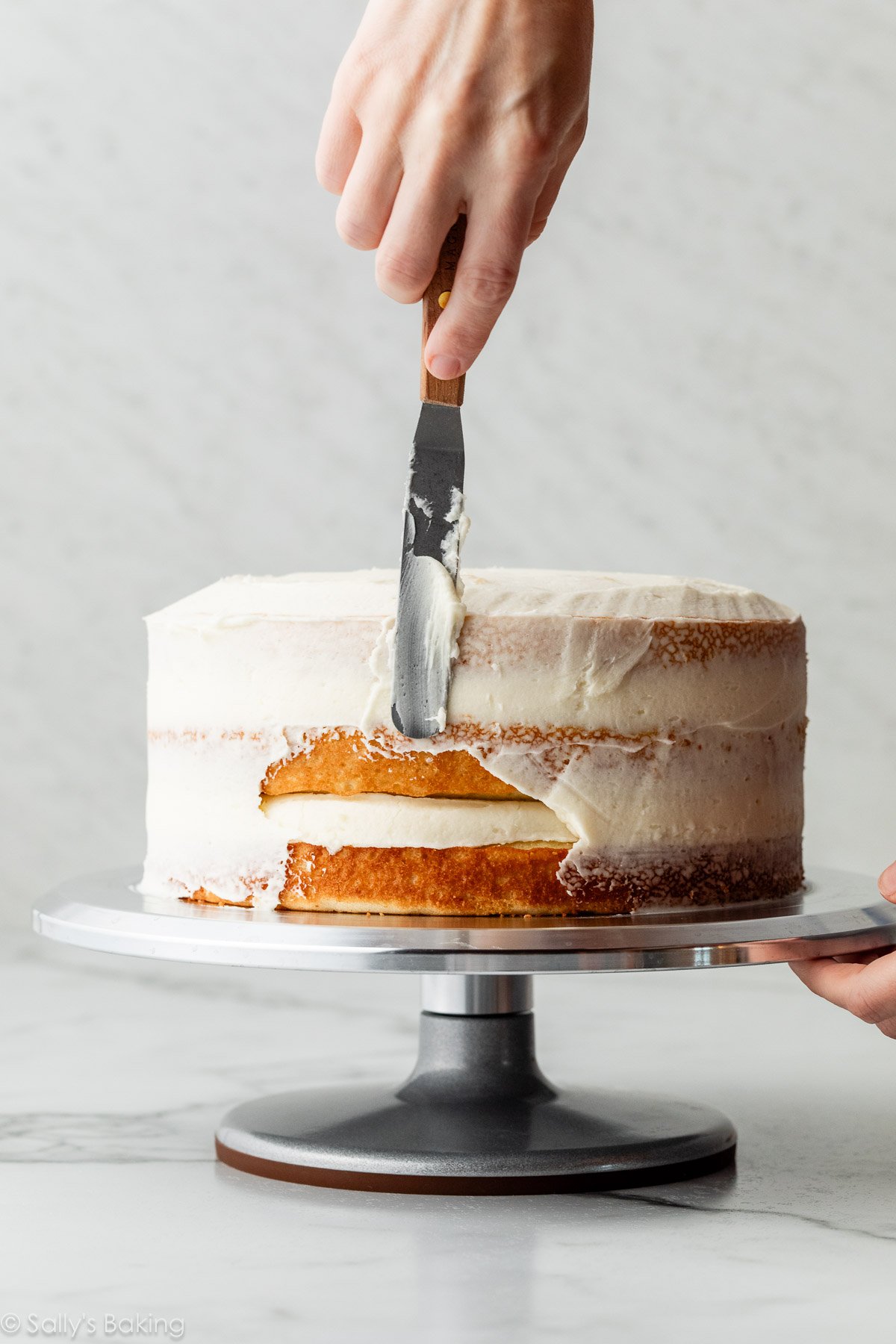 main étalant le glaçage de miettes sur un gâteau à étages.