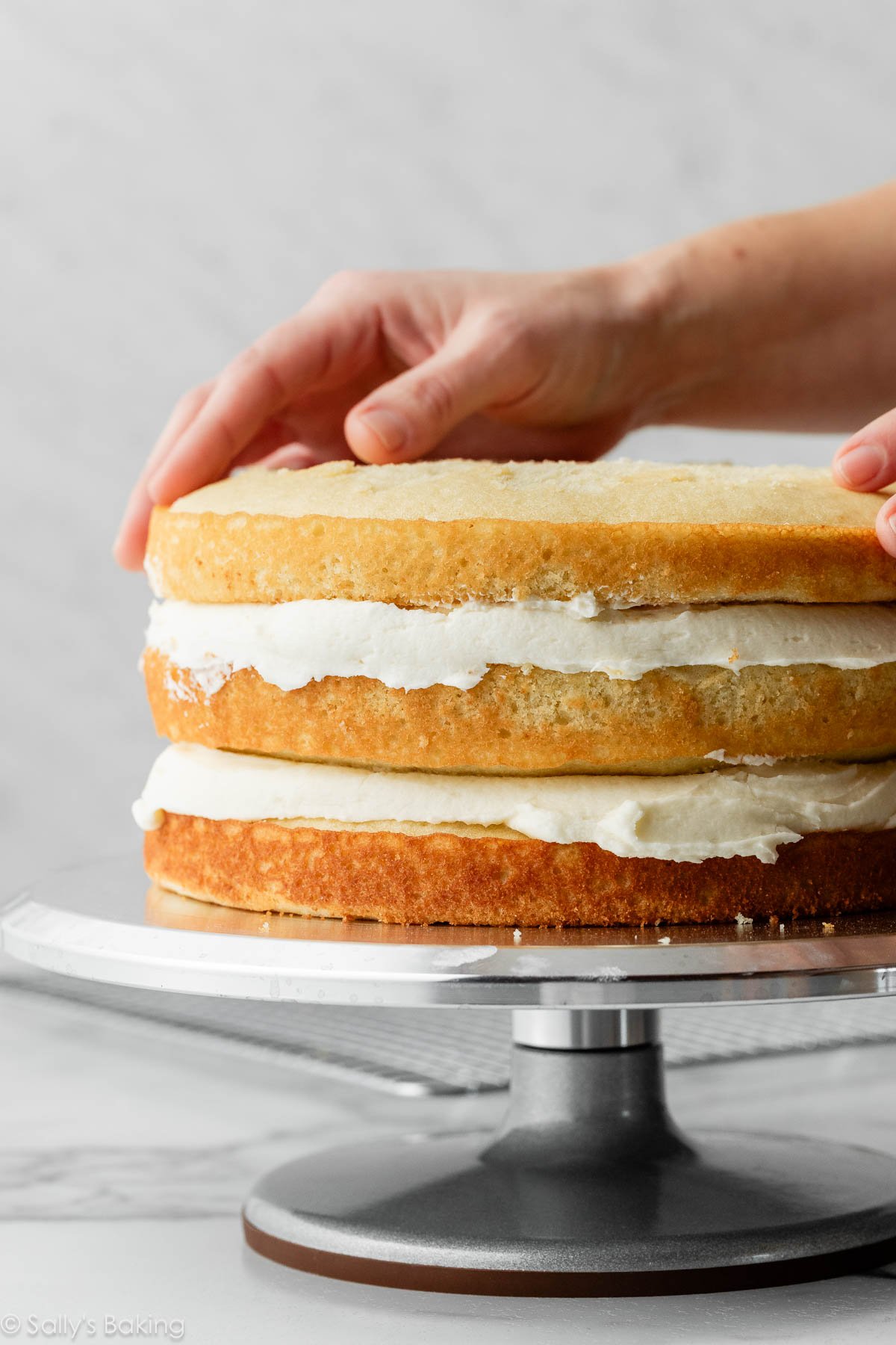 mains plaçant la 3ème couche de gâteau sur un gâteau.