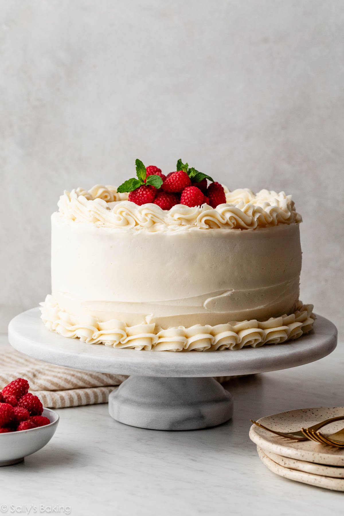 gâteau à étages vanille avec glaçage à la vanille et framboises fraîches et menthe sur le haut.