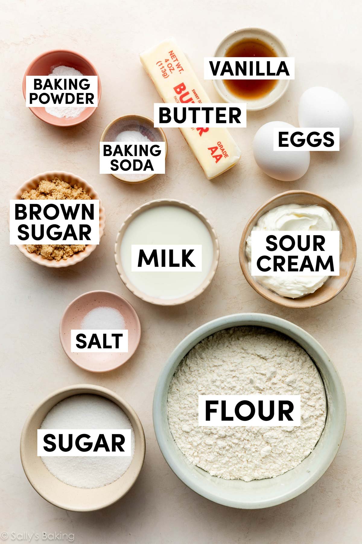 ingrédients sur une surface beige, y compris le sucre brun, la crème aigre, la farine, le beurre, la vanille et les œufs.