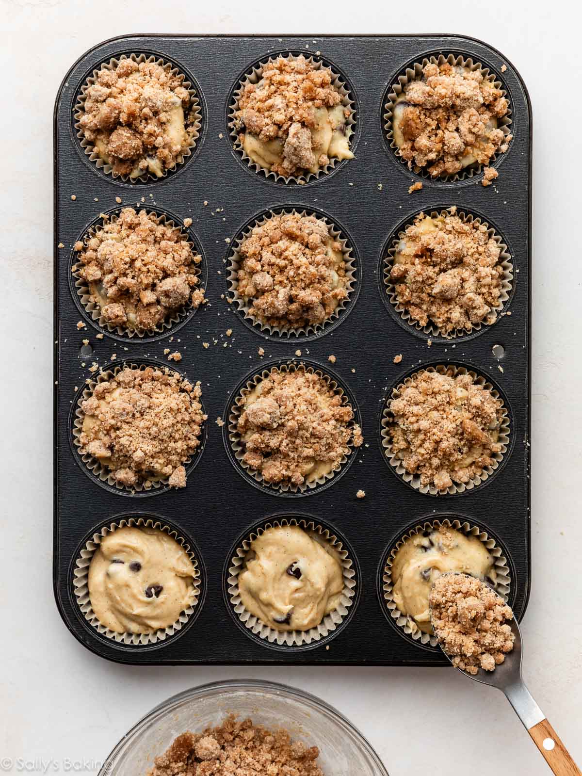 cuillère ajoutant de la garniture crumble à la pâte à muffins au chocolat.