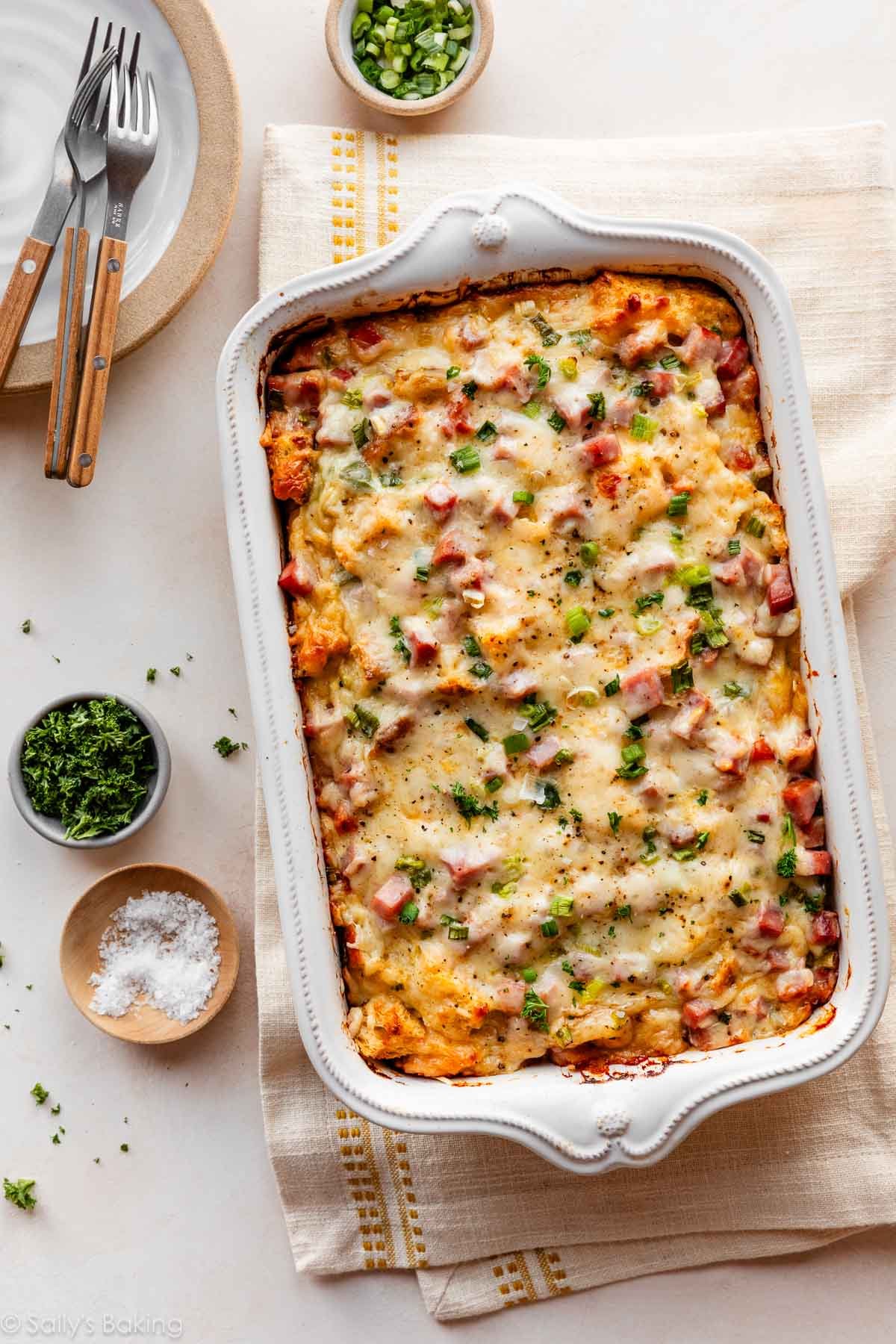 strata au jambon et fromage suisse dans un plat blanc avec de la ciboulette, du persil et du sel de mer.