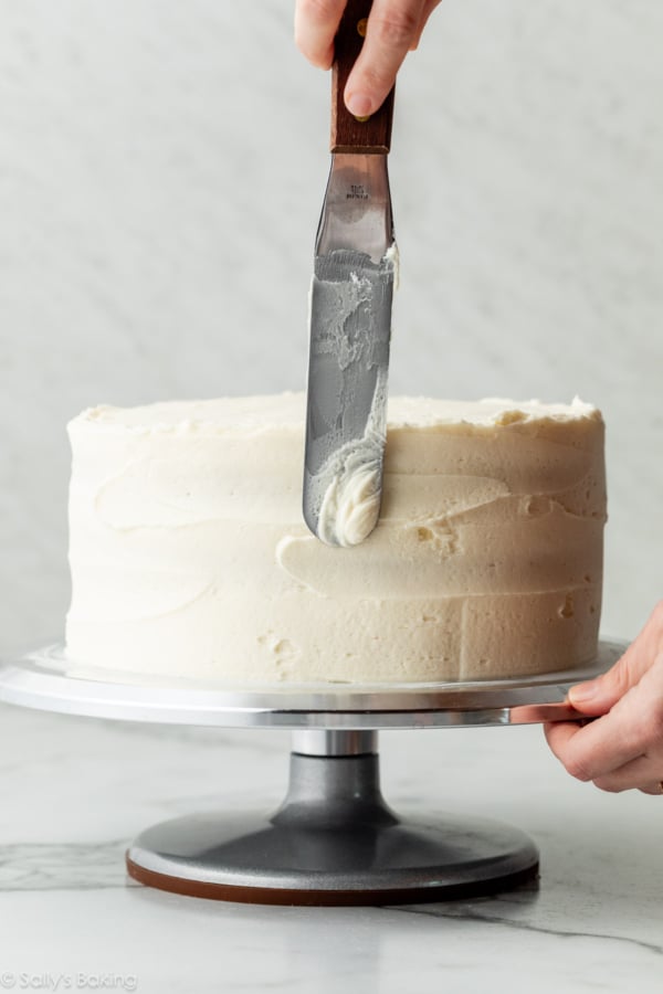 étalement de glaçage à la vanille sur un gâteau à étages avec une spatule.