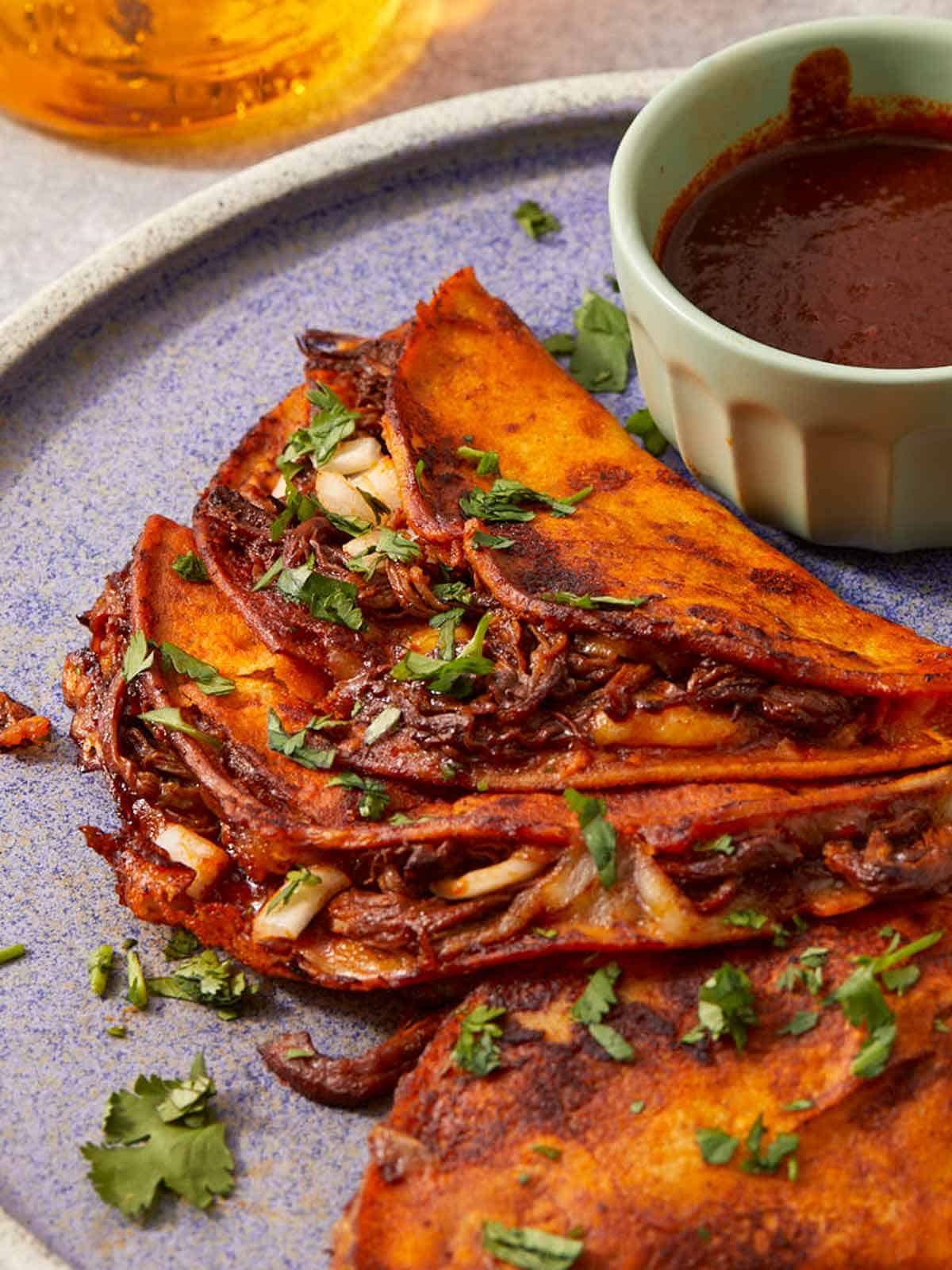 Gros plan sur des tacos birria croustillants servis avec un consommé.