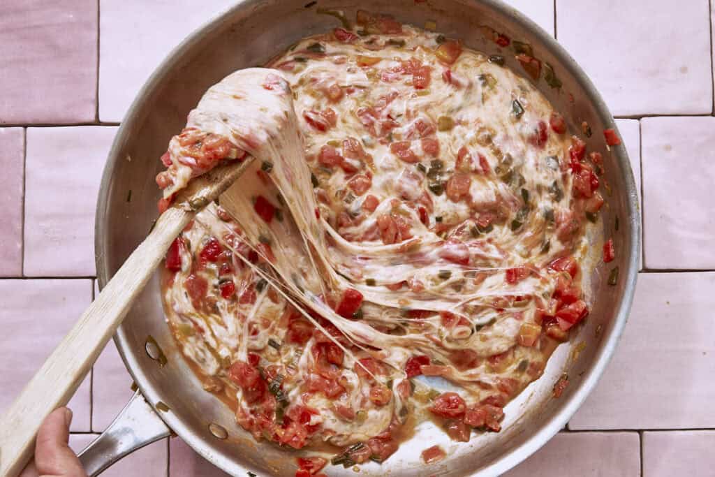 Mozzarella fondue s'étirant à travers une sauce tomate et oignon vert dans une poêle, remuée avec une cuillère en bois.