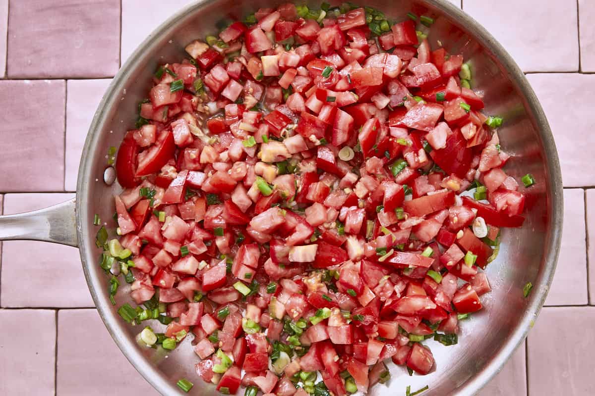 Tomates hachées et oignons verts cuisant dans une poêle en acier inoxydable.