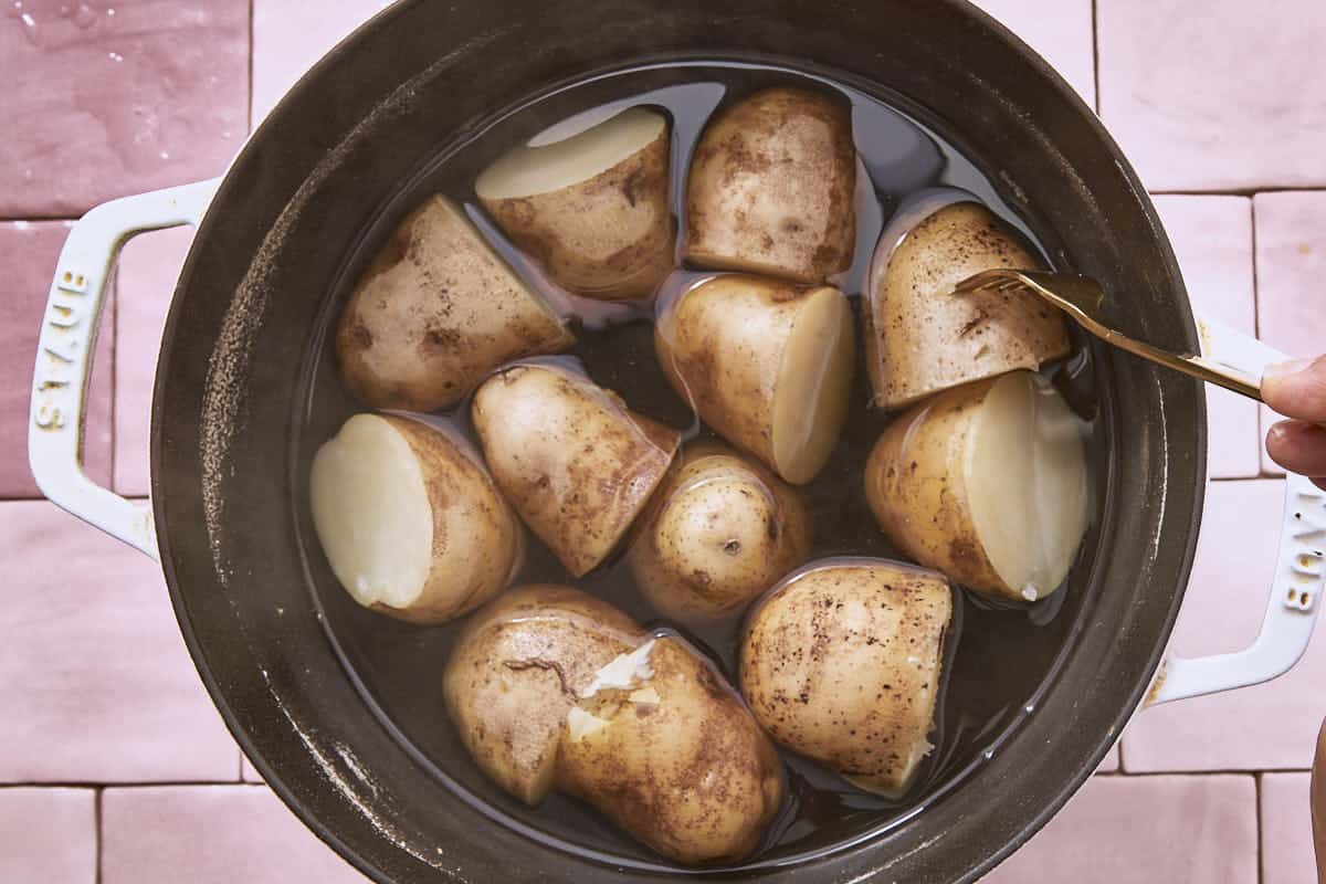 Pommes de terre coupées en deux bouillies dans une grande casserole, avec une fourchette.