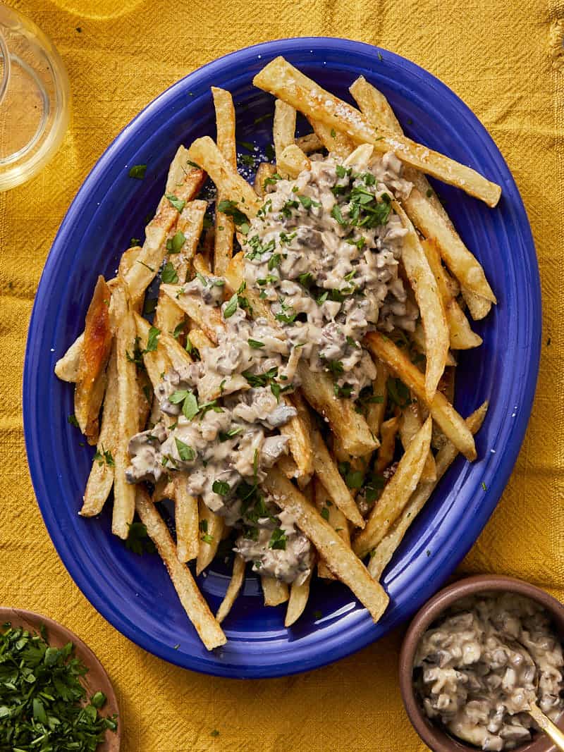 des frites croustillantes dans un bol bleu surmontées d'une sauce aux champignons et truffes avec du parmesan