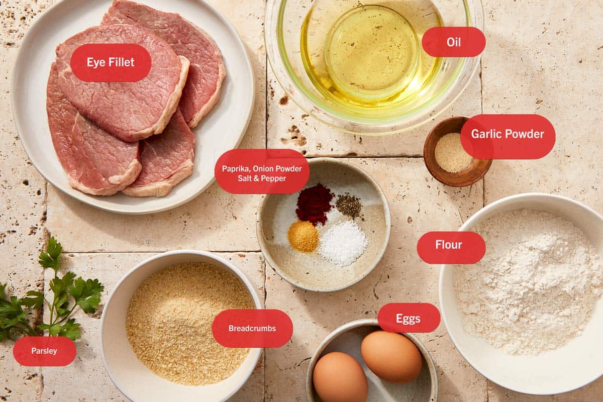 Steaks de filet de boeuf, œufs, farine, chapelure et épices disposés sur une planche en bois pour le beef milanesa.