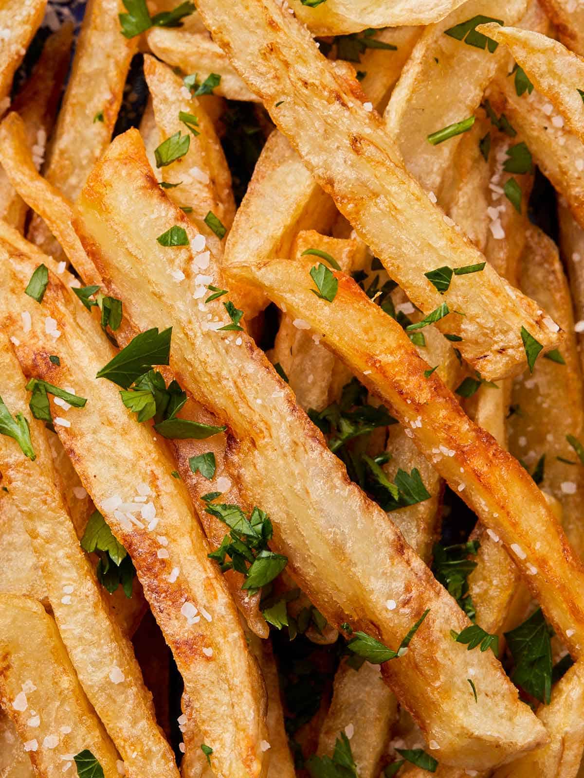 close up photo of crispy fries with salt and chopped parsley