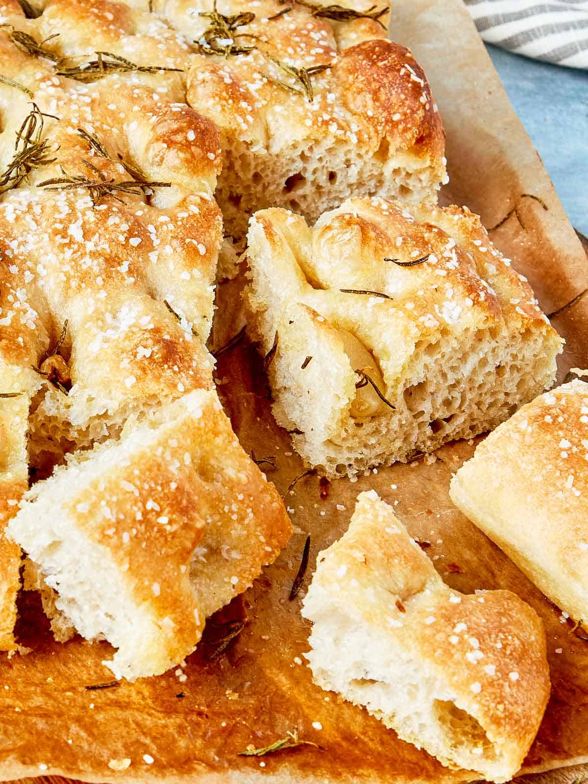 Gros plan sur la focaccia tranchée montrant une texture aérée, des bords croustillants et du romarin sur le dessus.