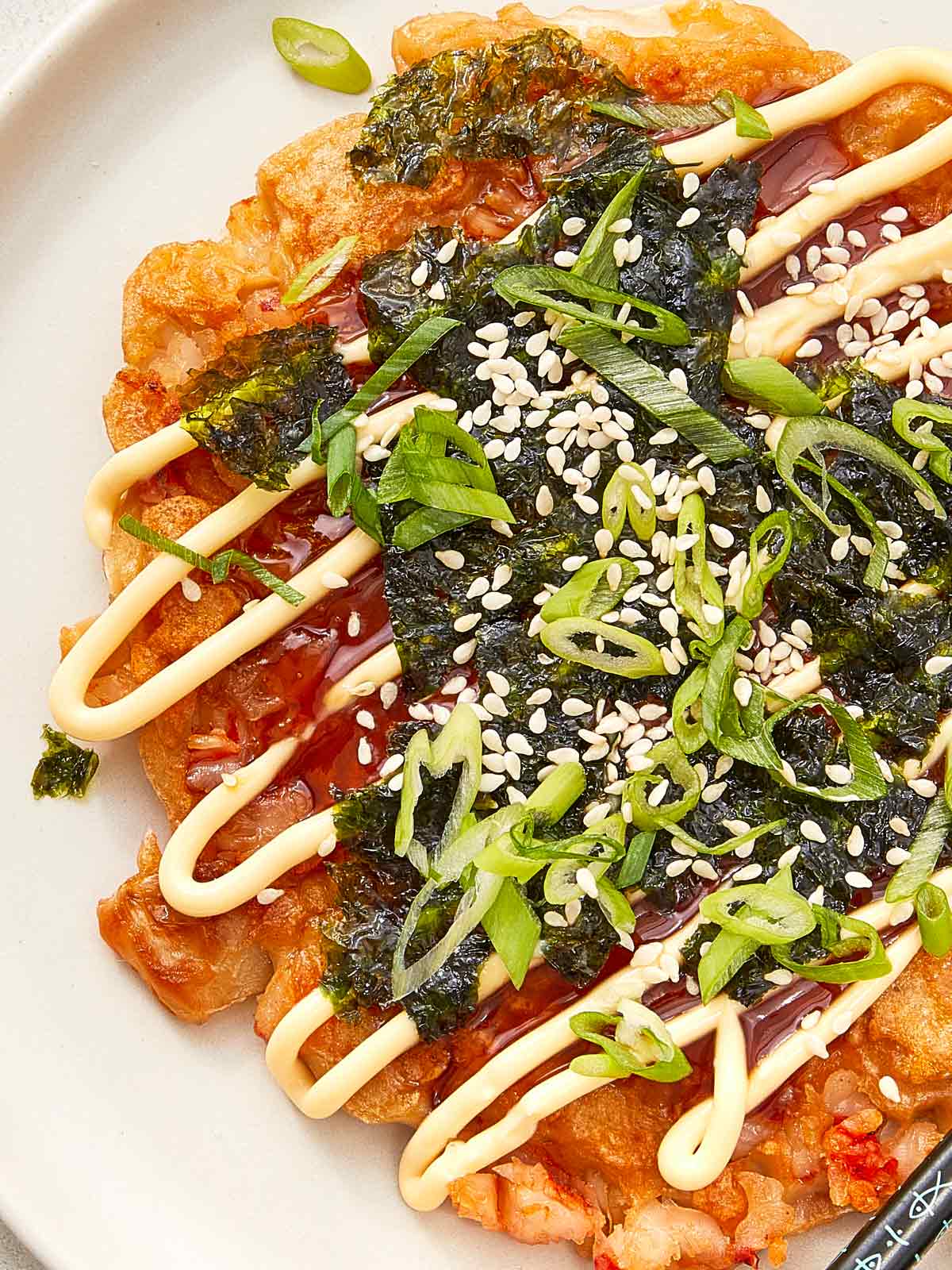Gros plan sur le pancake okonomiyaki garni de nori, d'oignons verts, de graines de sésame, et de filet de mayo et sauce.