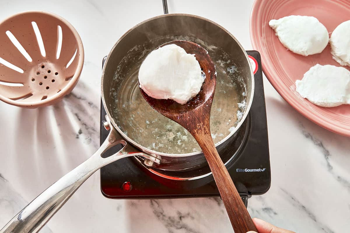 Un œuf poché soulevé de l'eau chaude avec une écumoire, entouré de parfaitement cuisinés sur une assiette.