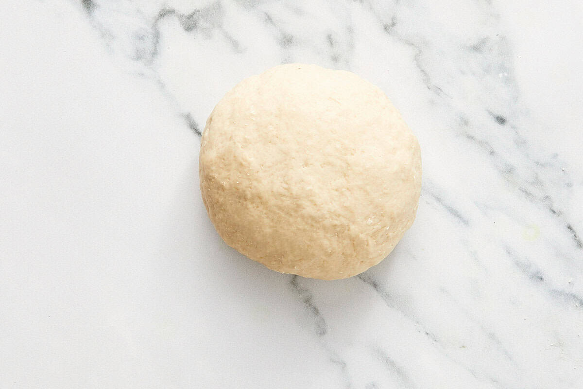 Boule lisse de pâte à bao sur une surface en marbre, prête à lever.