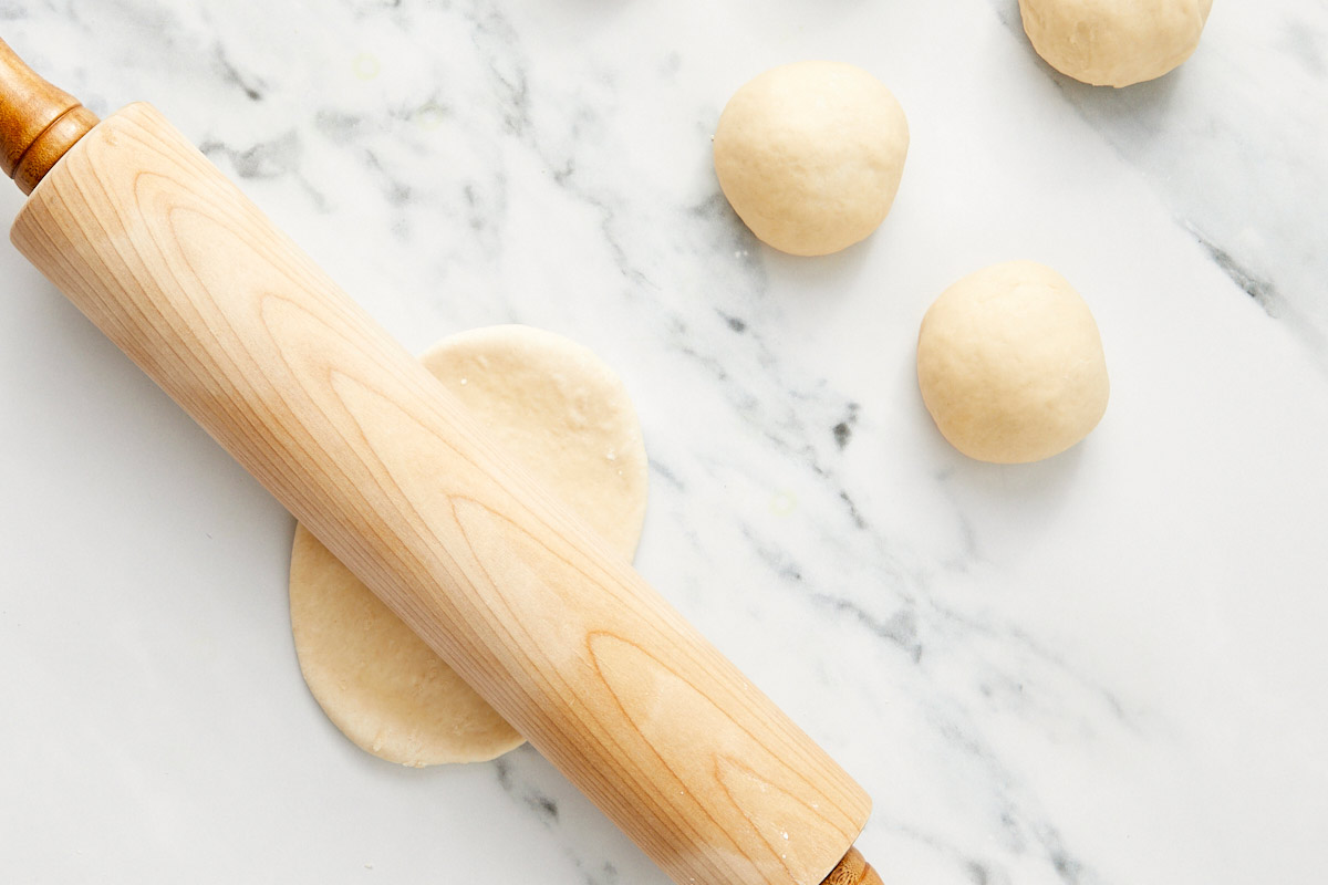 Petites boules de pâte à bao roulées en ovales avec un rouleau à pâtisserie en bois.