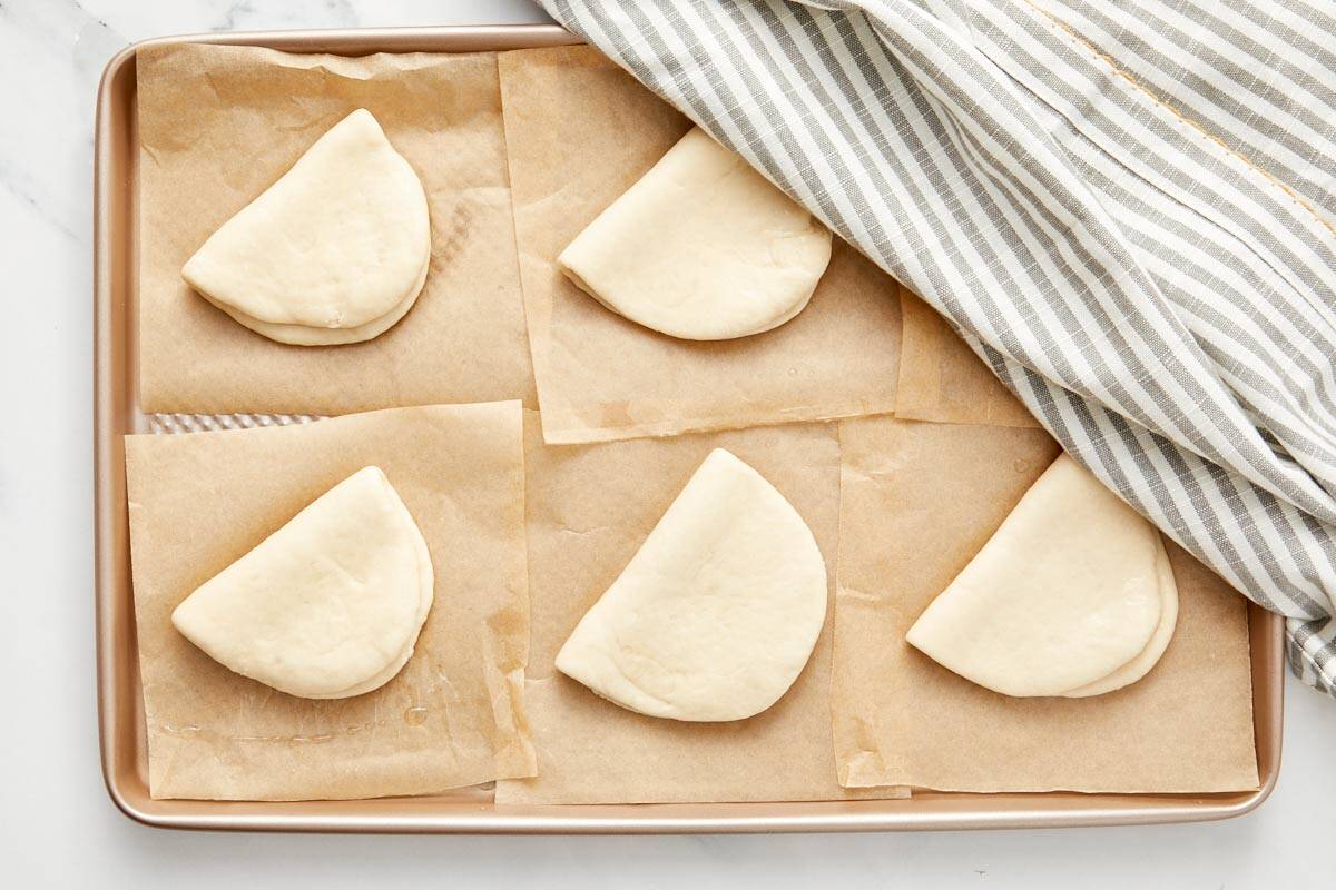 Brioches bao pliées reposant sur du papier sulfurisé, légèrement couvertes d'une serviette.