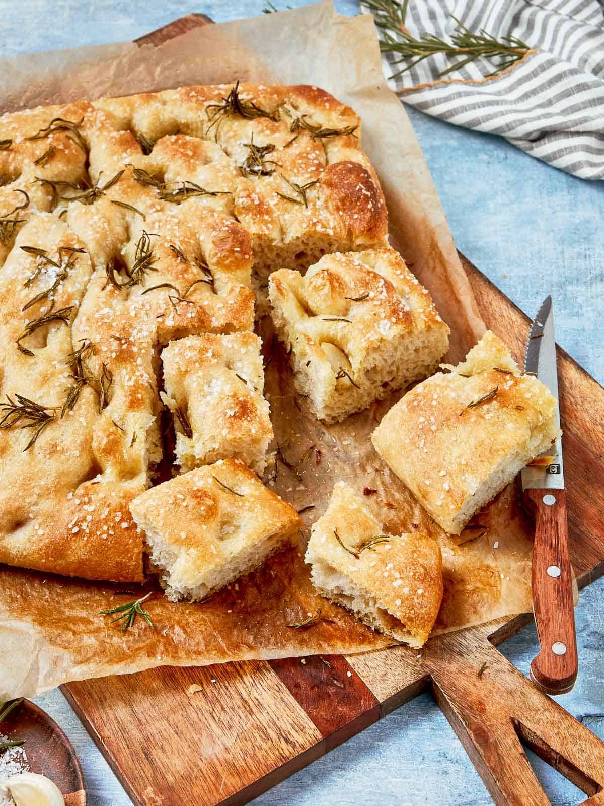 Focaccia cuite, coupée en carrés, couronnée de sel de mer et de romarin, servie sur du papier sulfurisé.