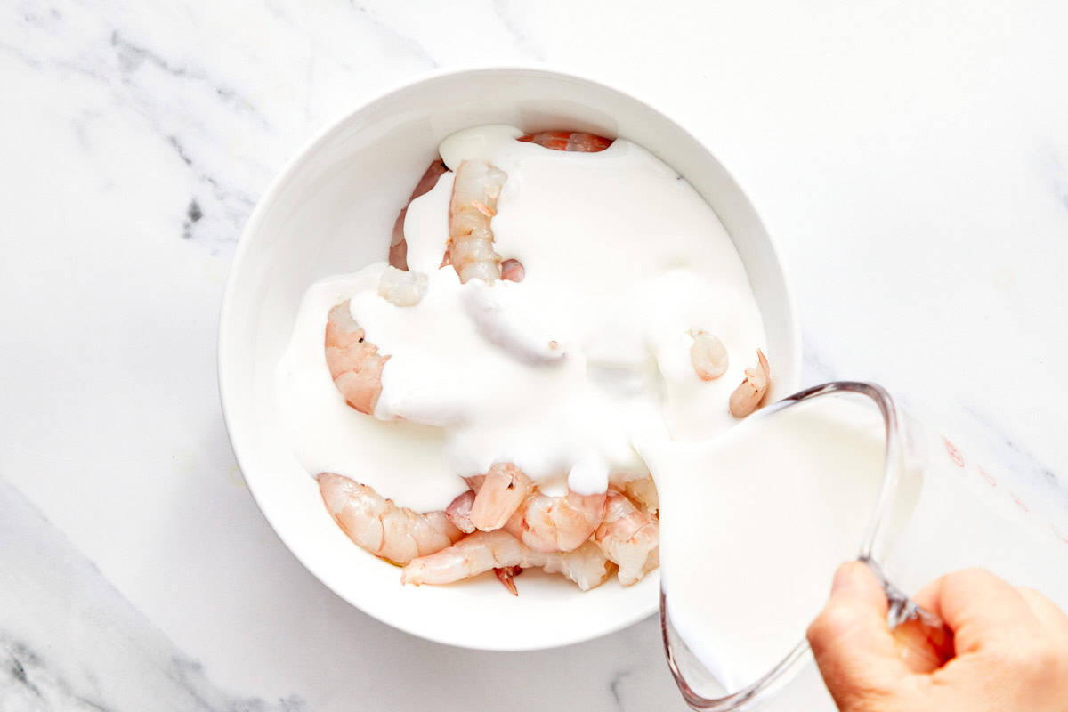 Crevettes crues dans un bol blanc avec du buttermilk versé dessus pour mariner.