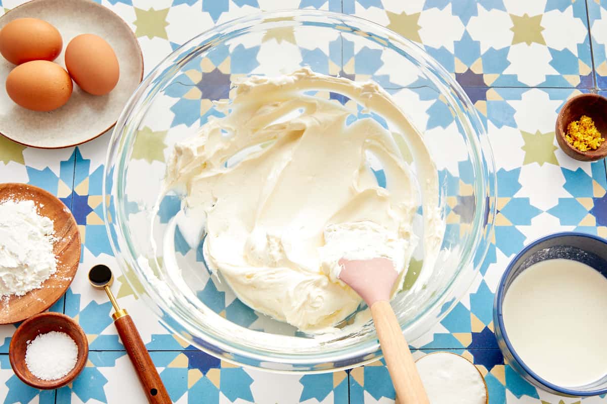 Fromage à la crème battu lisse dans un bol en verre avec des ingrédients de cuisson autour