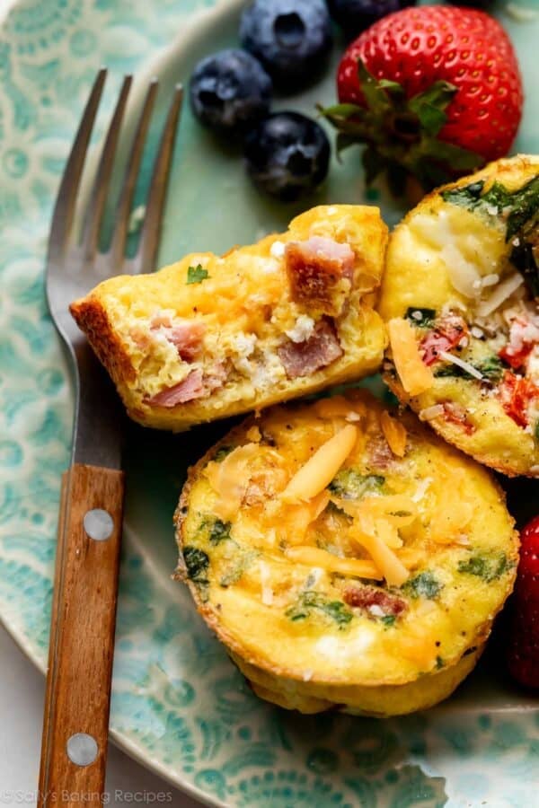 Muffins aux œufs et au jambon sur une assiette bleue avec des baies en arrière-plan.