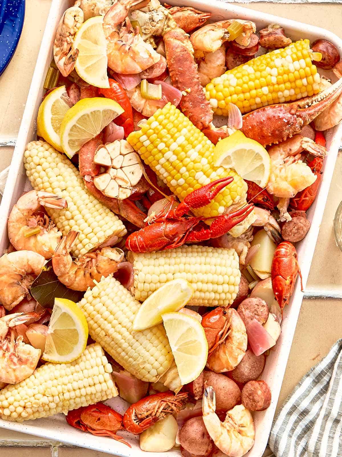 Vue de haut d'un plateau de bouillon de fruits de mer cuit avec du maïs, des crevettes, des pattes de crabe, des écrevisses, des pommes de terre, des saucisses, de l'ail et des quartiers de citron.