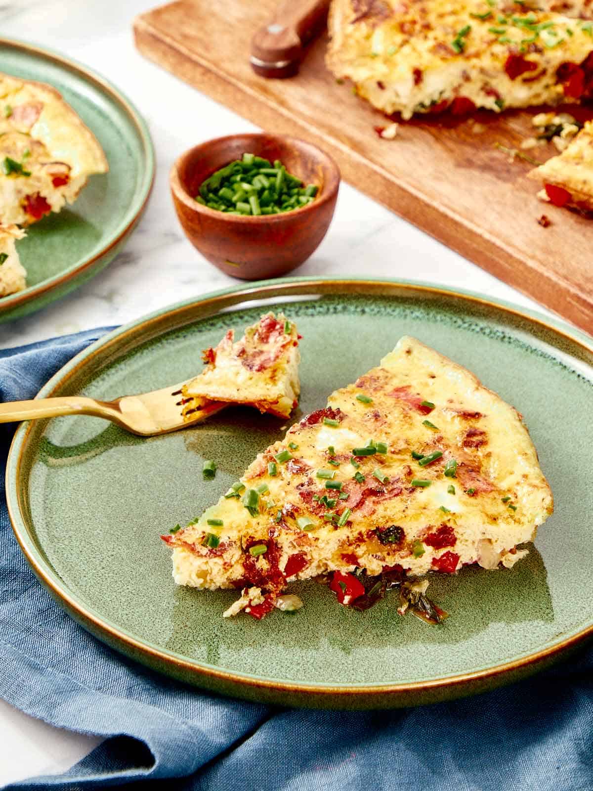 Une tranche de frittata servie sur une assiette en céramique verte, garnie de ciboulette fraîche.