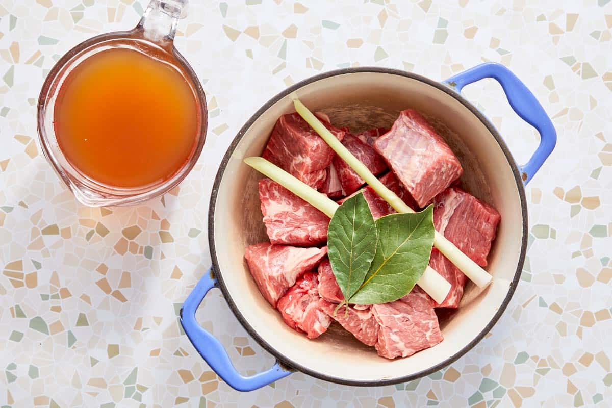 Morceaux de bœuf avec citronnelle et feuille de laurier dans une casserole avec du bouillon de bœuf.