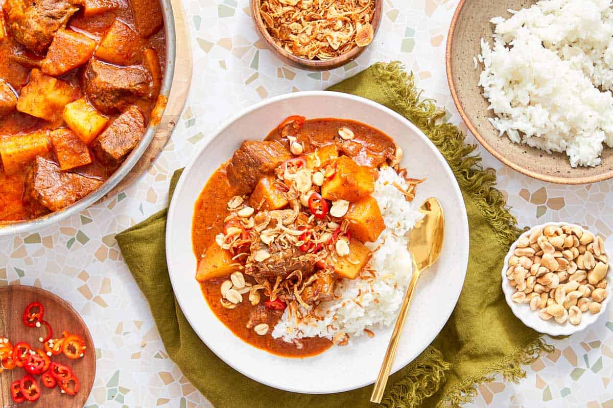 Curry de bœuf Massaman servi avec du riz jasmin, des cacahuètes et des échalotes croustillantes.