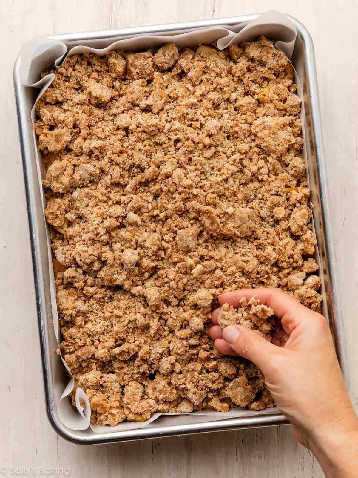 main saupoudrant le mélange de crumble sur la surface du gâteau.