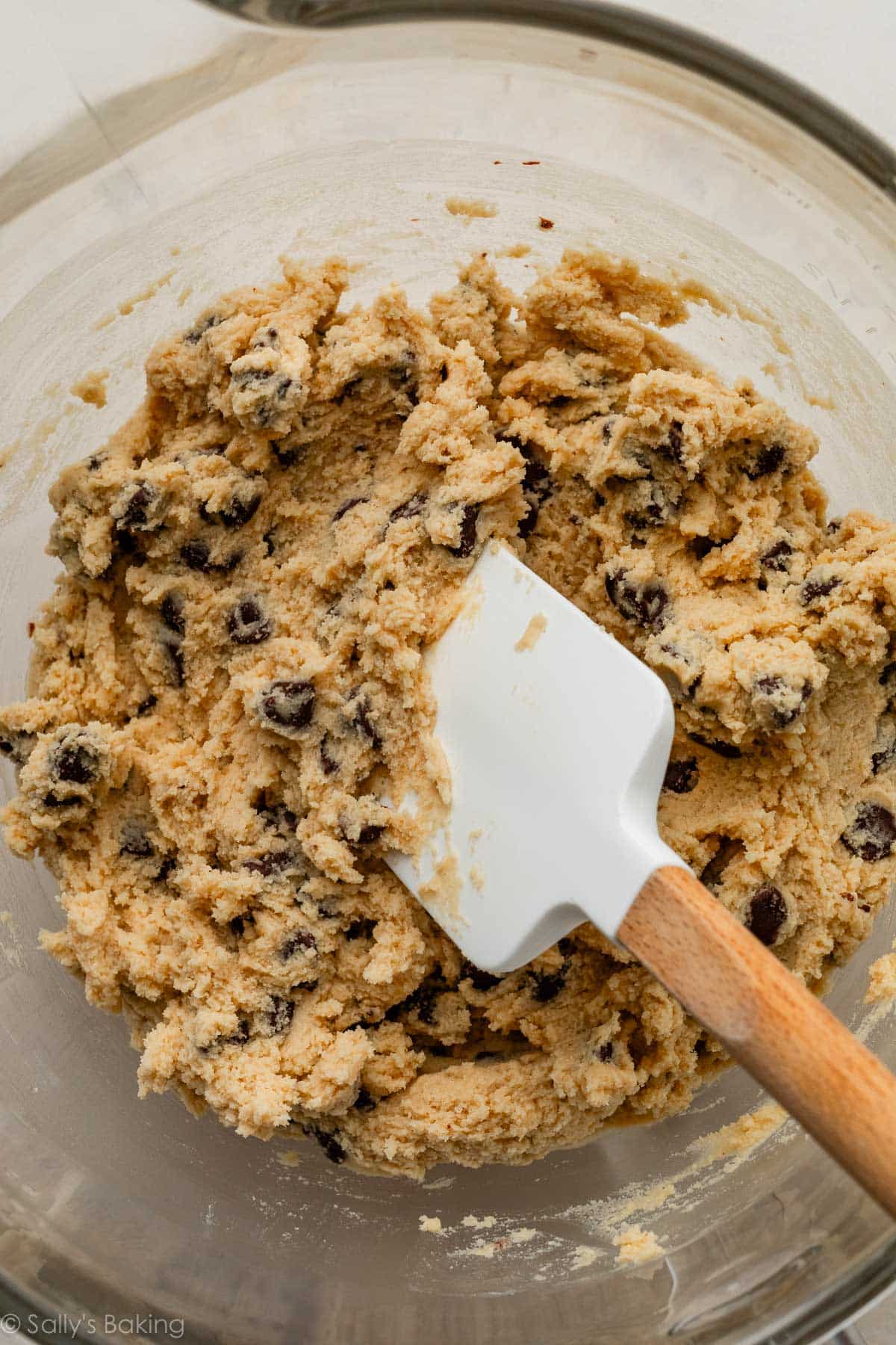 pâte à cookies dans un bol en verre avec une spatule blanche.