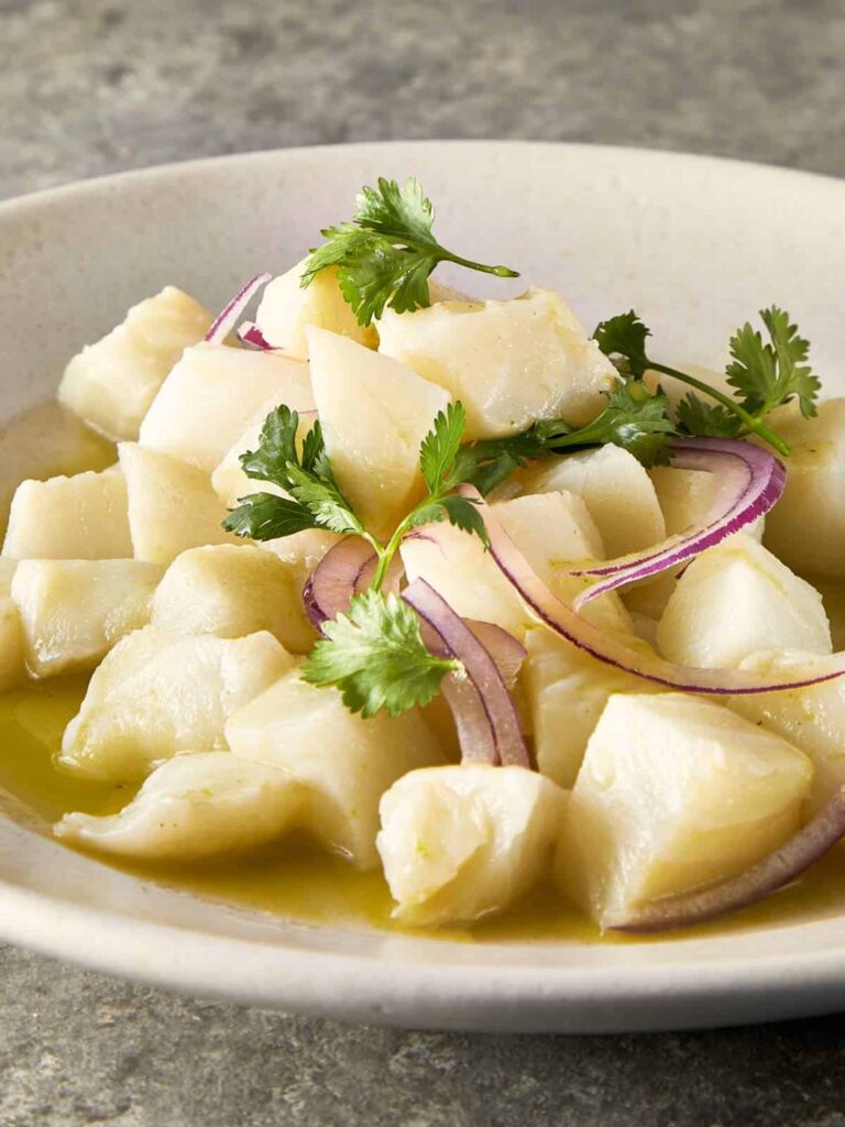 Close-up overhead view of fresh fish ceviche with red onion slices and coriander leaves.