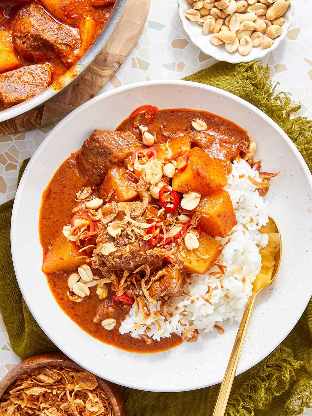 Curry de bœuf Massaman servi sur du riz jasmin, garni de cacahuètes et d'échalotes croustillantes.