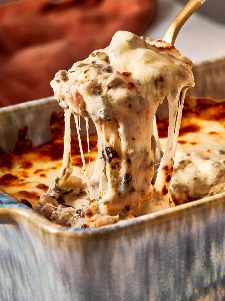 Spoon lifting hot, melted lasagna dip with gooey cheese.