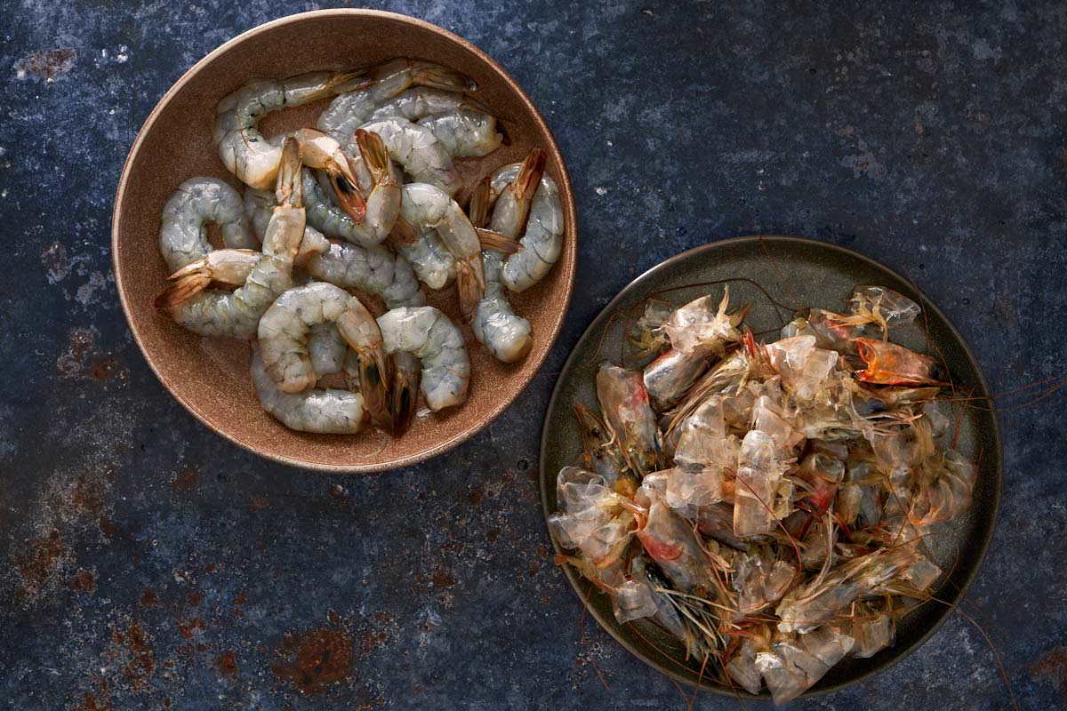 Crevettes crues décortiquées dans un bol, et coquilles et têtes de crevettes dans un autre, prêtes à faire le bouillon.