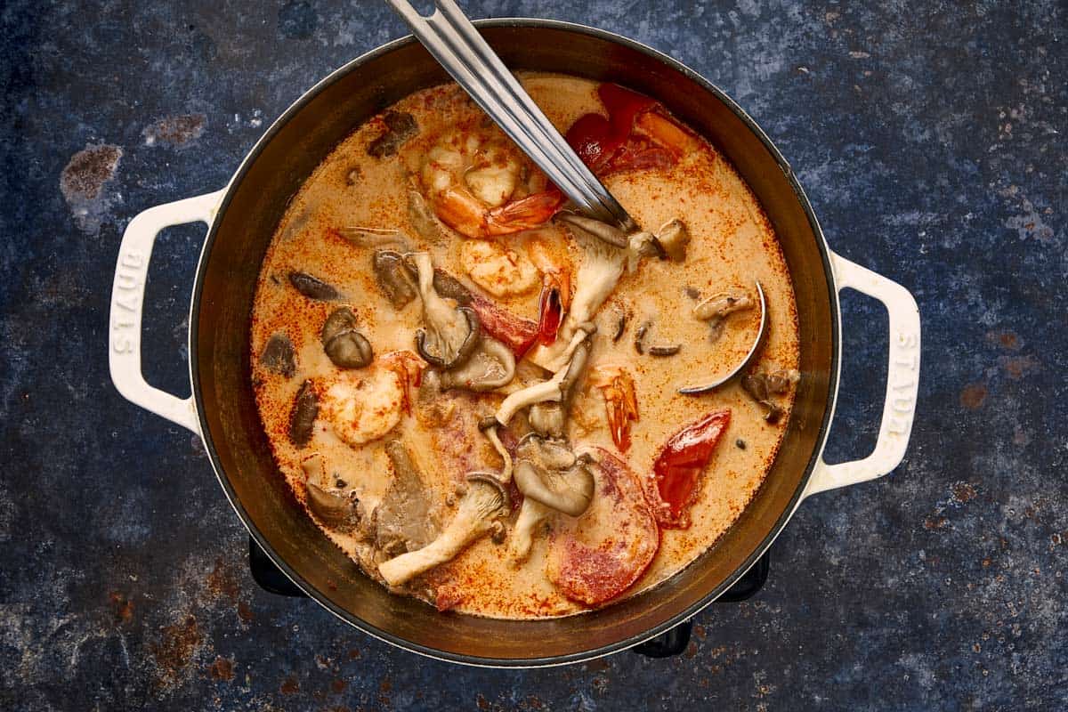Pot de soupe Tom Yum Kha crémeuse avec crevettes, champignons et tomates prêtes à être servies.
