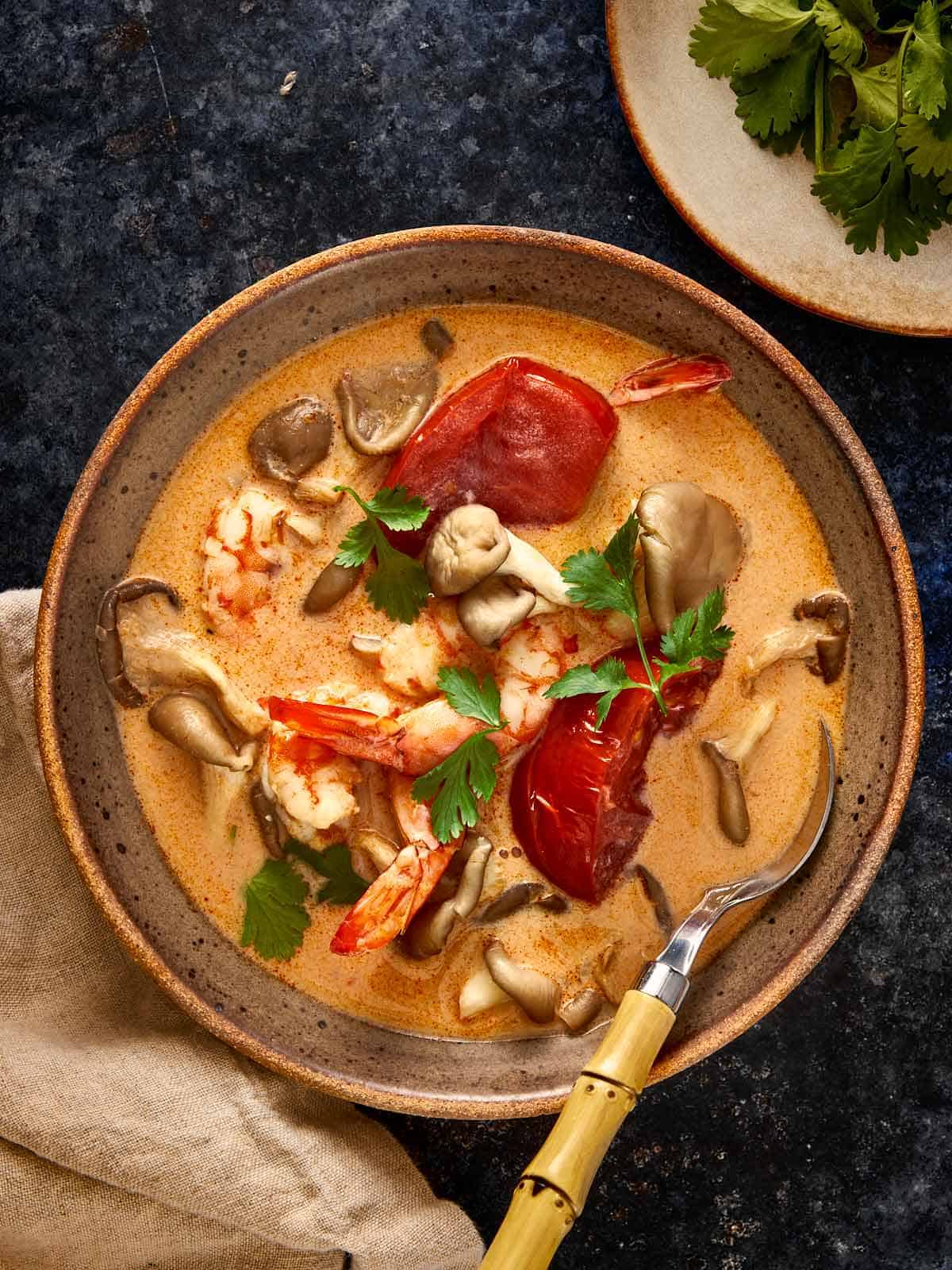 Un bol chaud de Soupe Tom Yum Kha avec crevettes, champignons et tomates dans un bouillon crémeux de coco, garni de coriandre fraîche.