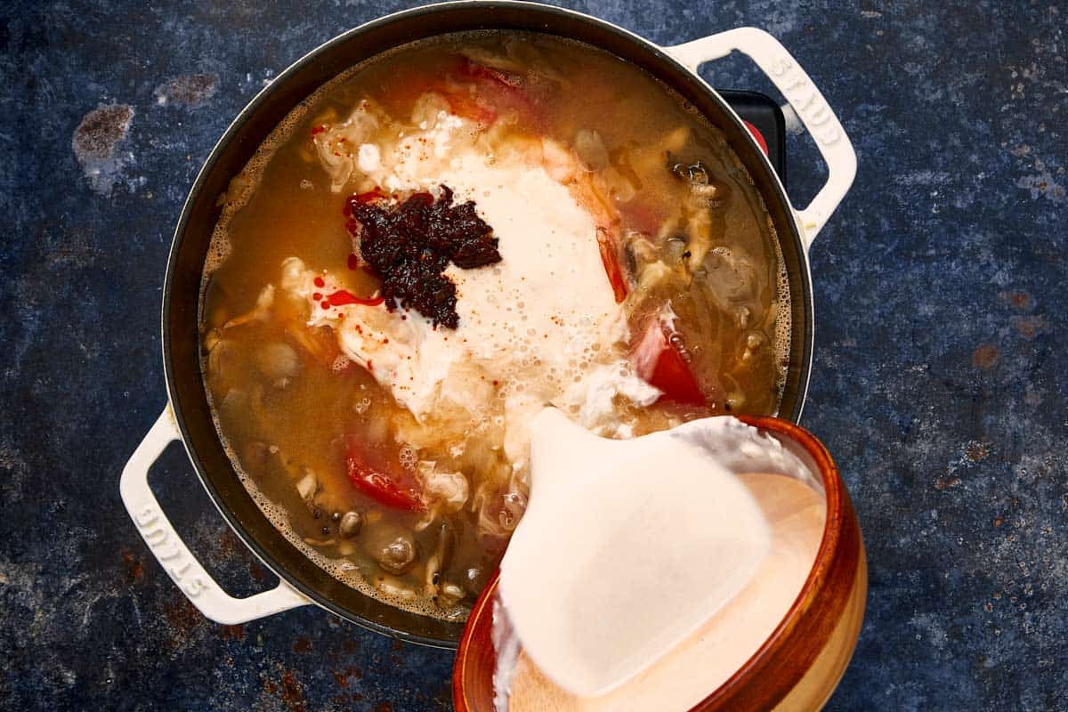 Versement de lait de coco et de pâte de piment thaïlandais dans un pot de soupe mijotante.