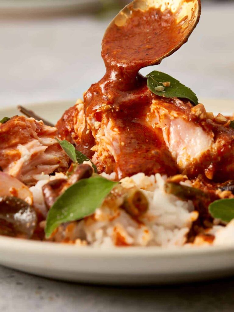 Close-up of golden curry sauce being spooned over salmon and rice, highlighting the creamy texture, kaffir lime leaves, and glossy finish of the Panang curry.