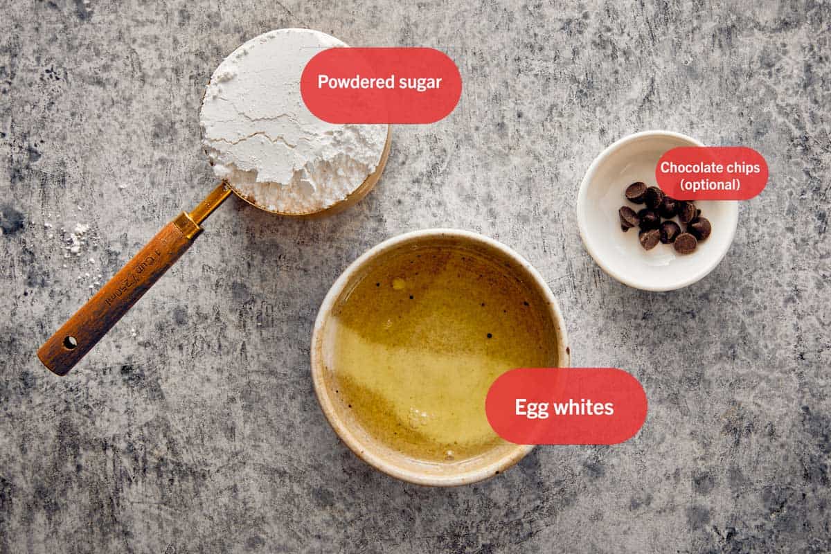 Ingrédients pour les Fantômes Suisses en Meringue, y compris le sucre glace, les blancs d'œufs et des pépites de chocolat.